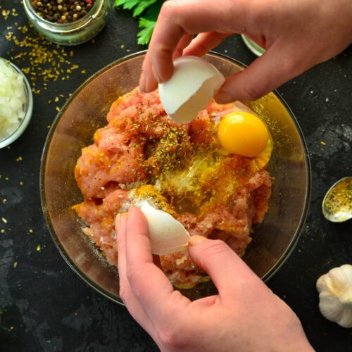 Cooking process. Minced meat and ingredients, salt, pepper, spices, onions, eggs, parsley, mix the ingredients with a spoon. A woman is preparing minced chicken for meatballs. Top view.