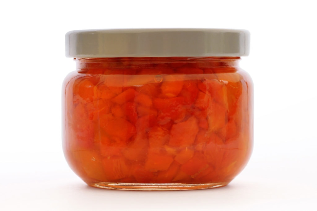 Bright red jar of canned pimentos on a white background
