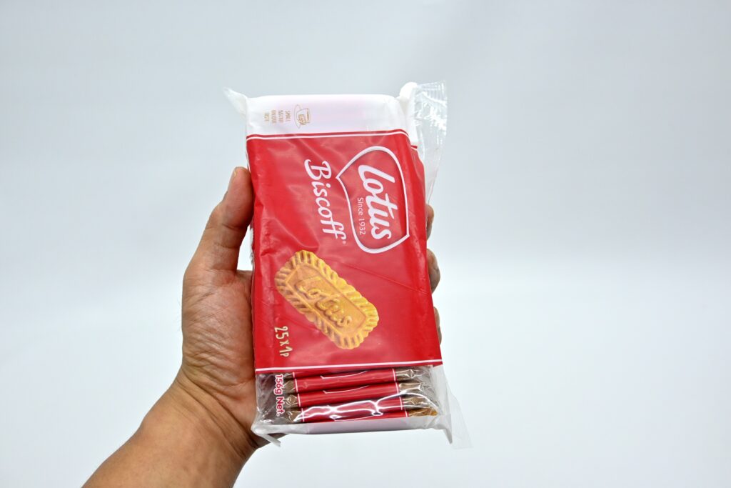 A person's hand is holding a Lotus Biscoff biscuit