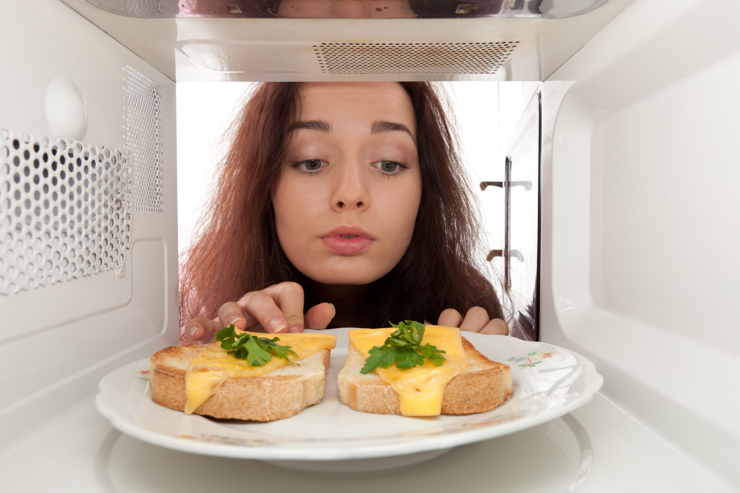 a girl look inside the microwave with two bread and cheddar cheese